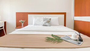 A neatly made bed with white linens, a wooden headboard, and a decorative pillow. A small table with a vase of flowers and a candle is beside the bed. - Good And Comfy 2Br At Springlake Summarecon Bekasi Apartment (Bekasi)
