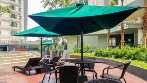 Un espace extérieur aménagé avec des chaises et des tables en osier, des parasols verts et un escalier menant à un bâtiment.
