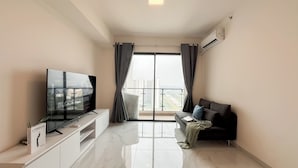 A modern living room with a flat-screen TV, a sofa, a coffee table, and a balcony with curtains. - Cozy 2Br With Extra Room At Sky House Bsd Apartment (Pagedangan)