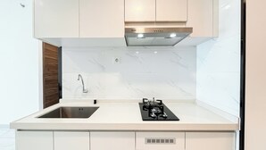 A modern kitchen with white cabinets, a stainless steel sink, a gas stove, and a built-in oven. - Cozy 2Br With Extra Room At Sky House Bsd Apartment (Pagedangan)