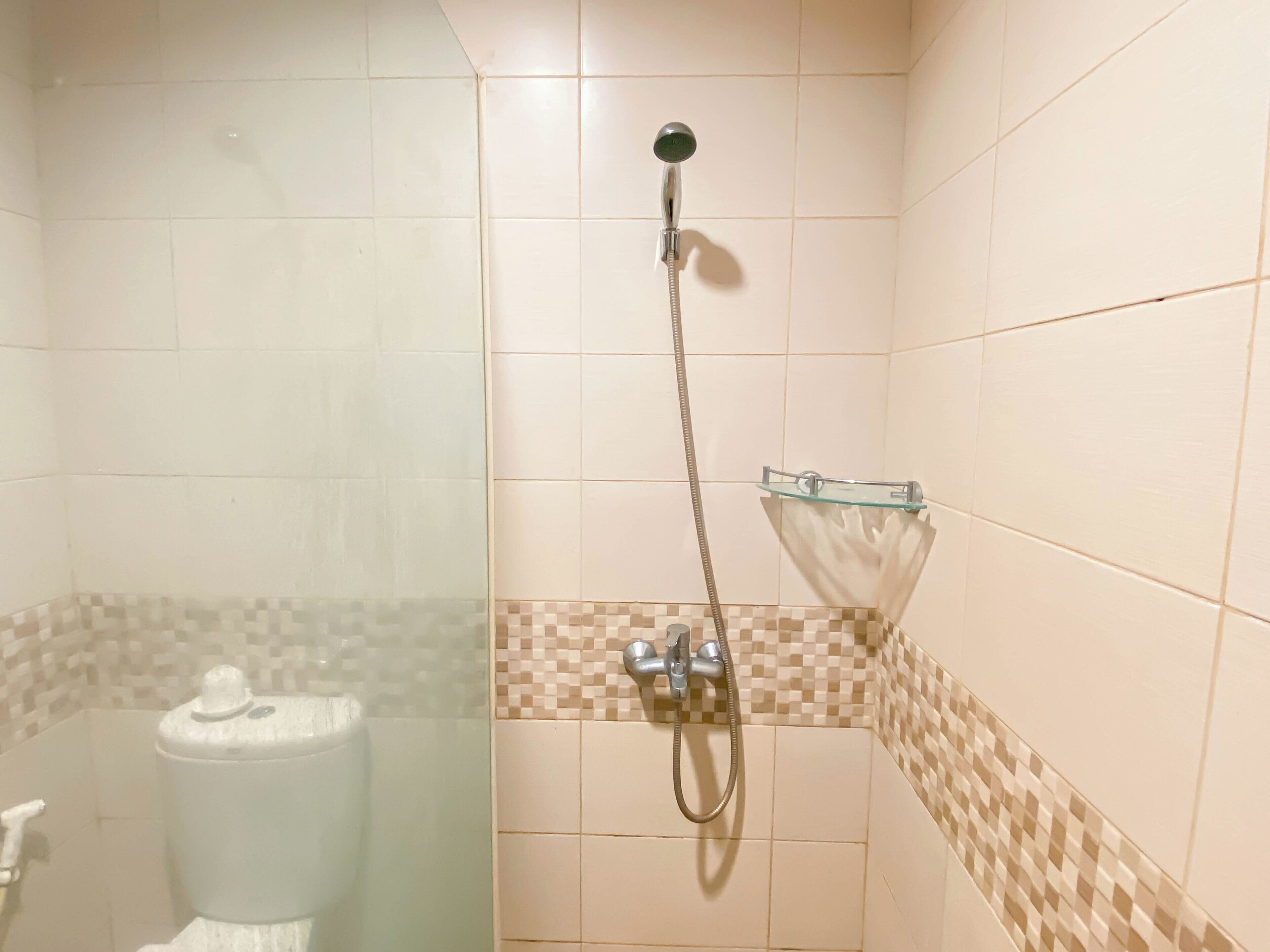A shower area with a glass enclosure, a handheld showerhead, and a tiled wall with a checkered pattern.