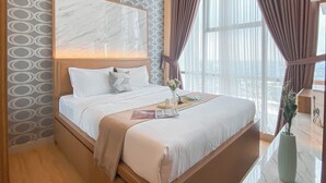A modern hotel room with a large bed, a marble headboard, a view of the city, and a large window with curtains. - Good Deal 1Br Tamansari Iswara Apartment (Bekasi)