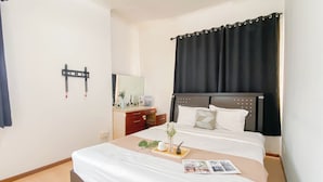 Ein Hotelzimmer mit Bett, Nachttisch, Schminktisch und einem großen Fenster mit Vorhängen.
