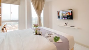 A hotel room with a bed, a TV mounted on the wall, a window with curtains, and a balcony with a view. - Cozy And Enjoy Studio At Tokyo Riverside Pik 2 Apartment (Teluknaga)