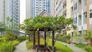 A residential area with a gazebo surrounded by greenery, tall apartment buildings in the background, and a paved pathway. - Gorgeous And Homey 1Br Apartment At Podomoro City Deli Medan (Medan)