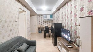 A living room with a sofa, a television, and a kitchen area in the background. - Gorgeous And Homey 1Br Apartment At Podomoro City Deli Medan (Medan)