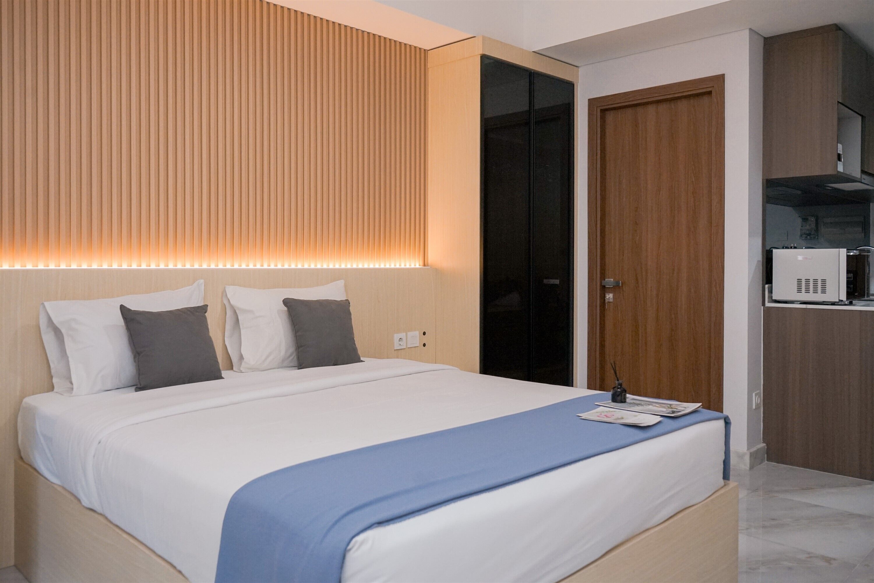 A modern hotel room with a large bed, a wooden headboard, a microwave, and a wardrobe.