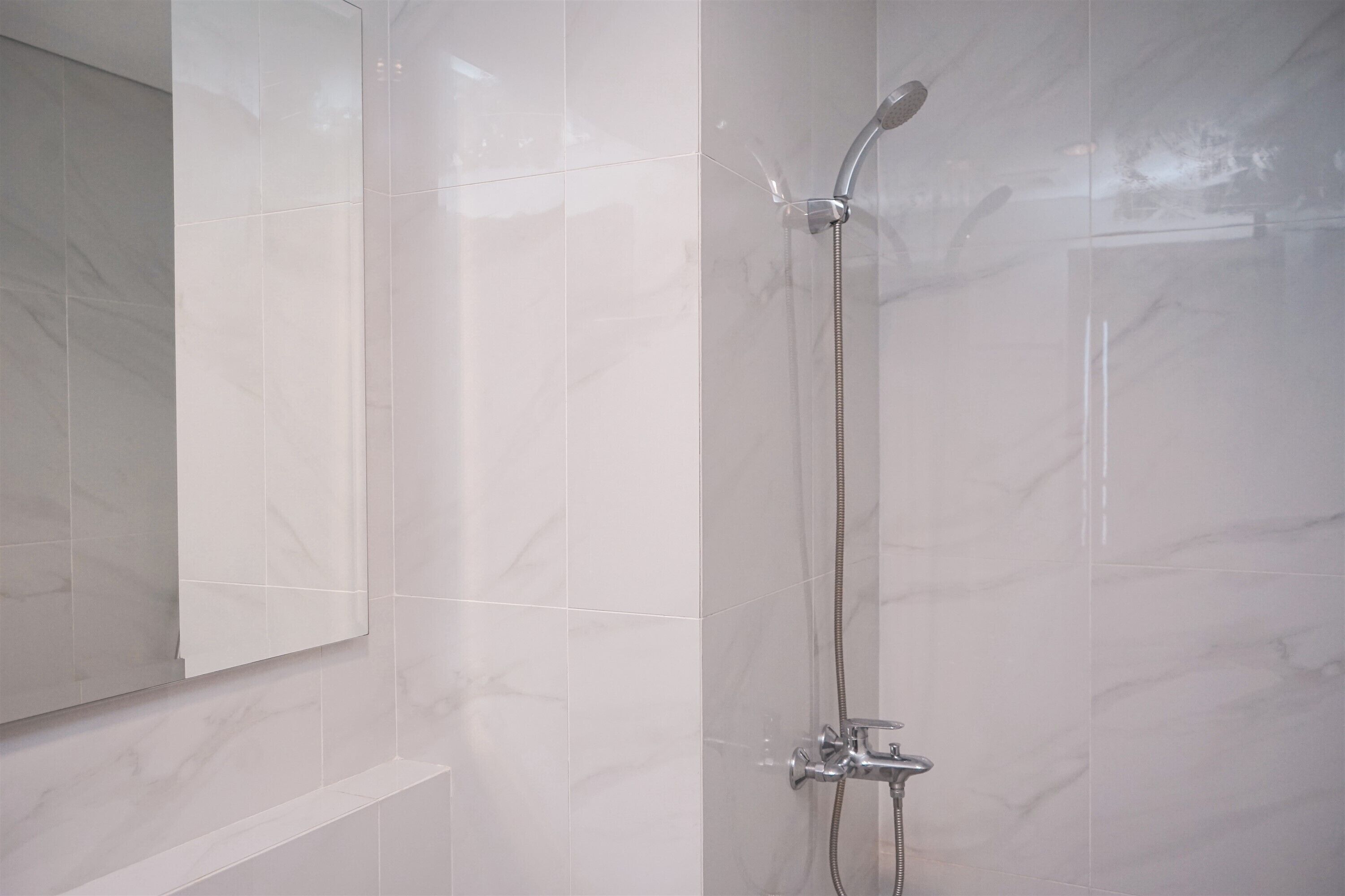 Une douche équipée d’un pommeau de douche à main et d’un robinet fixé au mur.