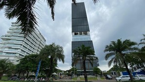 A tall, modern skyscraper with a glass facade, surrounded by palm trees and other greenery. - Spacious Studio At Apartment The Smith Alam Sutera (Tangerang)