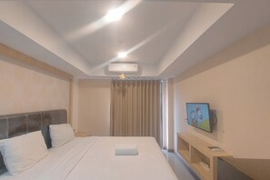 A hotel room with a bed, a flat-screen TV, an air conditioning unit, and a window with curtains. - Best Deal Studio At De Prima Apartment (Medan)