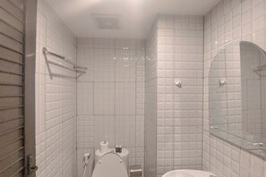 Un baño con paredes de azulejos blancos, un inodoro, un lavabo y una cabina de ducha de vidrio.