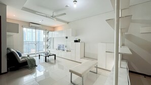 A modern, well-lit living room with a sofa, a coffee table, and a bench. There is a large window providing a view of the cityscape. - Nice And Cozy 3Br Apartment At Thamrin Residence (Jakarta)