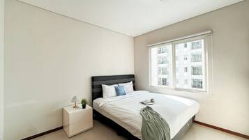 Un dormitorio con una cama, una mesita de noche, una ventana y vistas a un edificio.