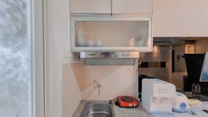 Una cucina compatta con lavello in acciaio inossidabile, forno a microonde, bilancia rossa e dispenser d'acqua.