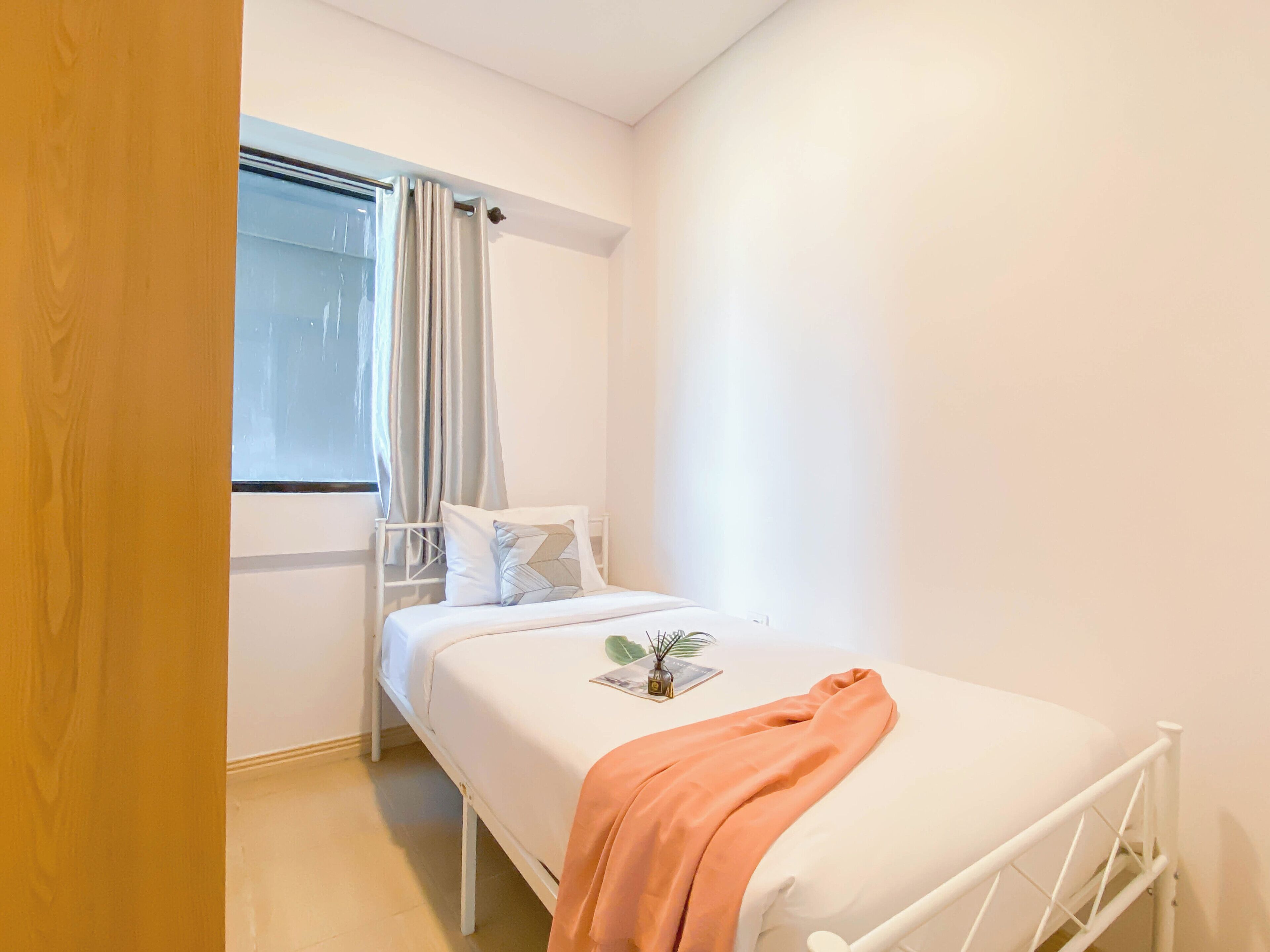 A bedroom with a bed, a window with curtains, and a bedside table with a plant.