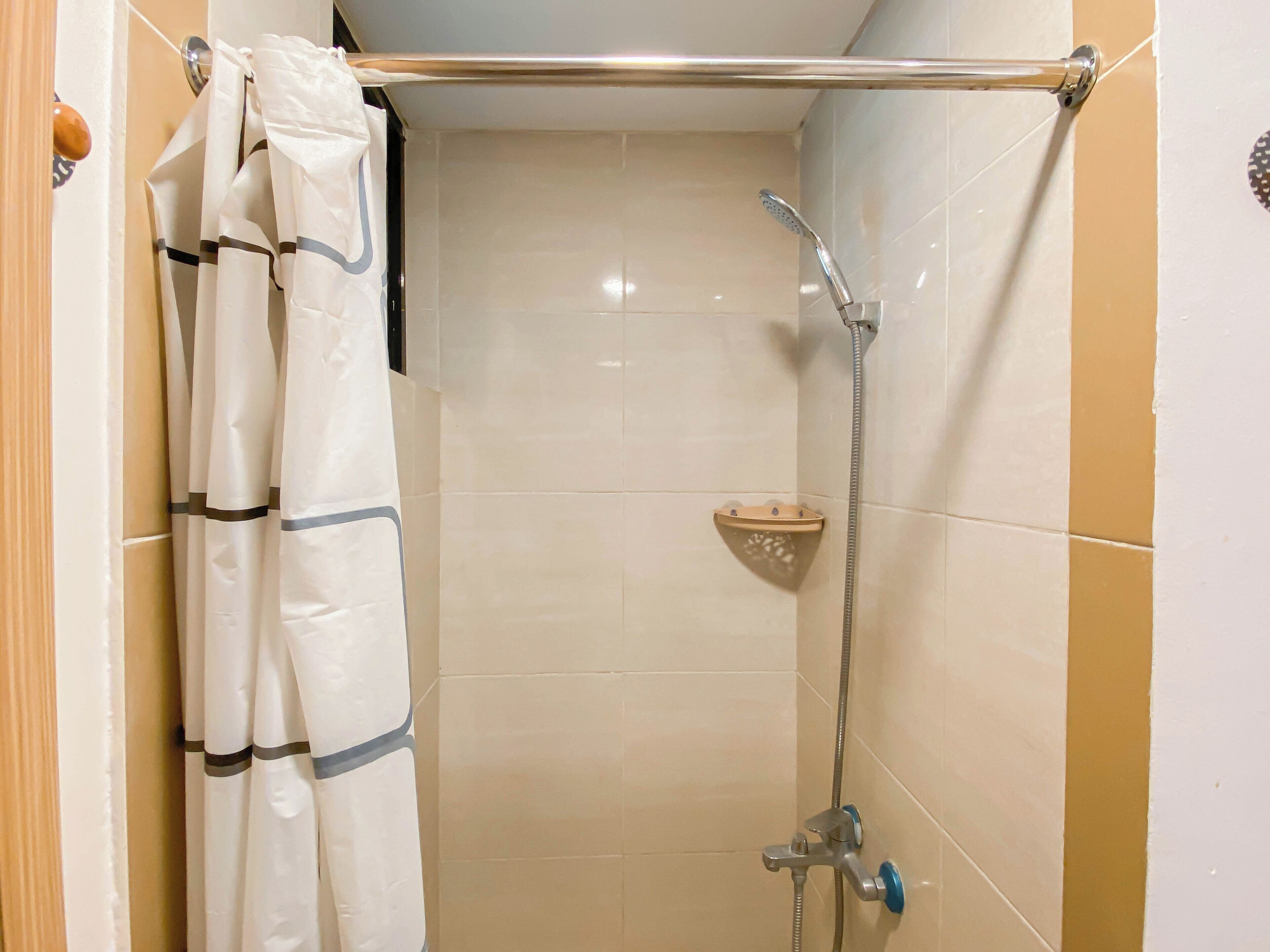 A shower area with a handheld showerhead, a towel bar, and a small shelf.