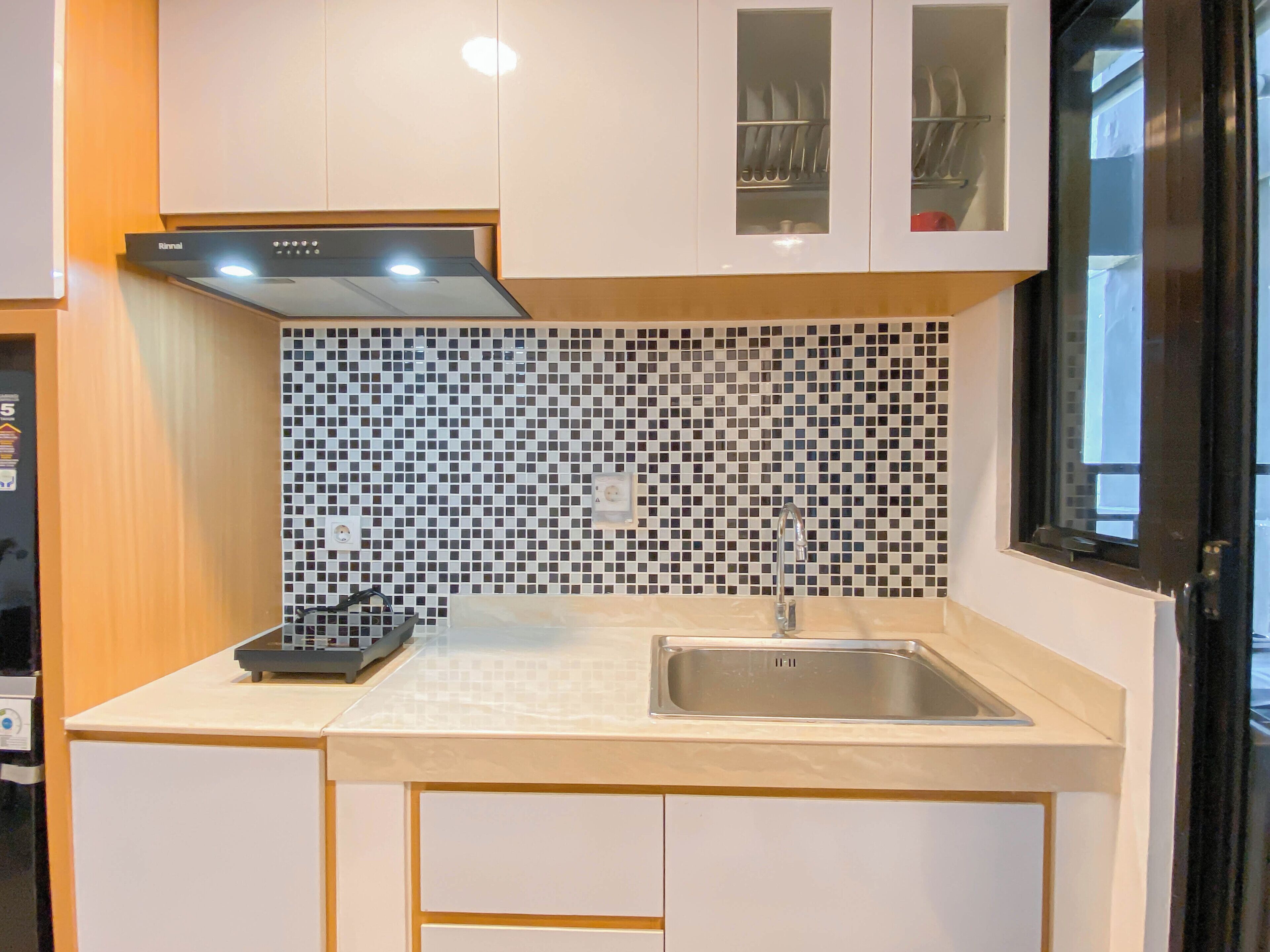 Een compacte keuken met een modern ontwerp, met een zwarte Rinnai inductiekookplaat, een roestvrijstalen spoelbak en een betegelde achterwand.