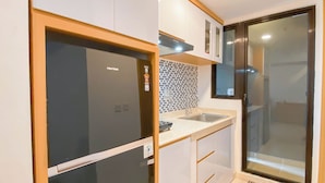 A compact kitchen with a refrigerator, sink, and tiled backsplash. - Comfy Stay 2Br At Meikarta Apartment (Cikarang)