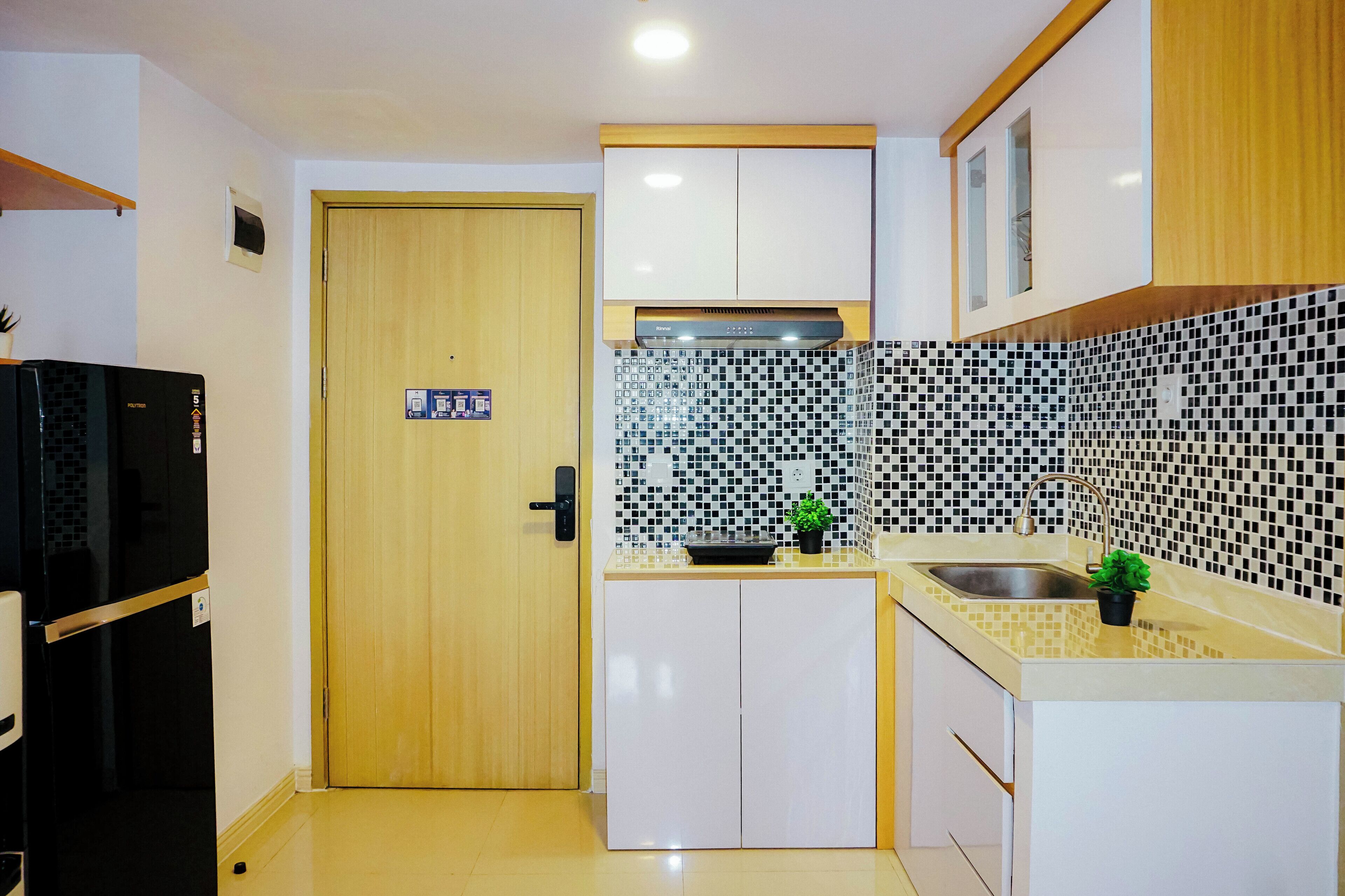 A compact kitchen with a wooden door, a black refrigerator, white cabinets, a tiled backsplash, and a sink.