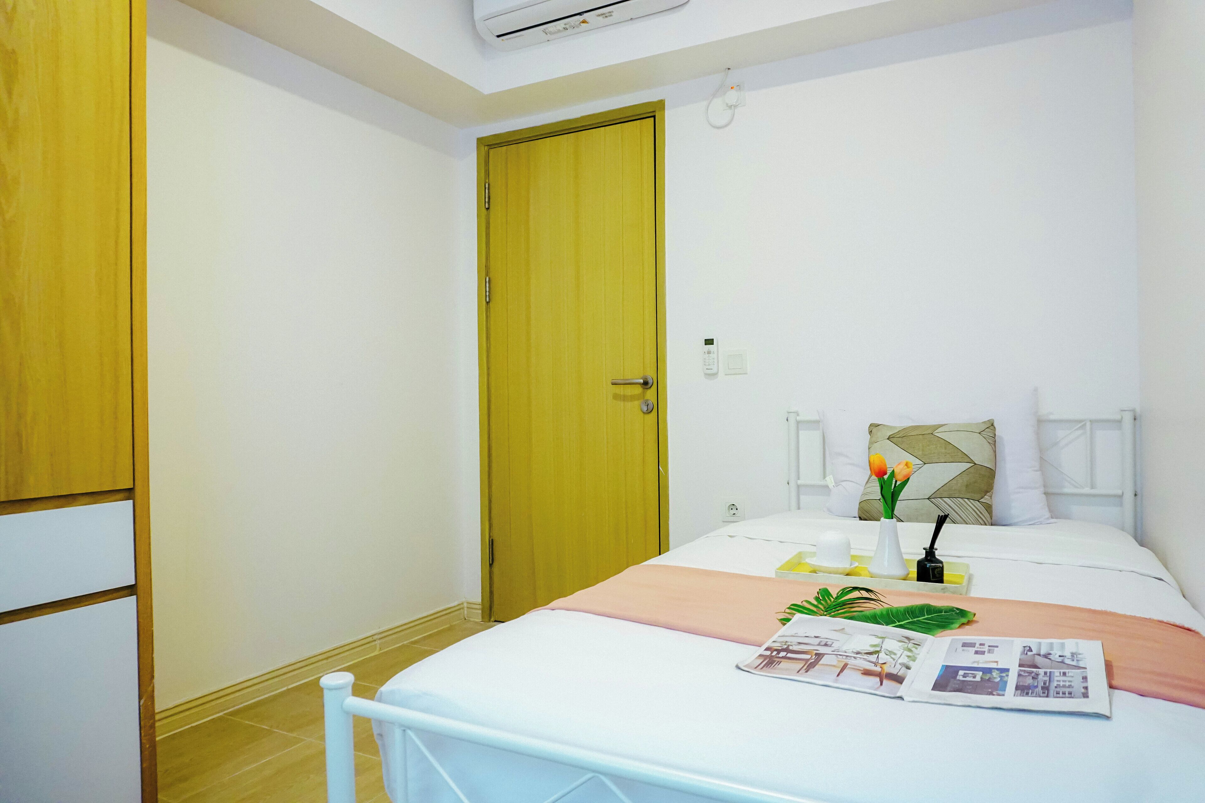 Habitación de hotel con cama, puerta de madera, radiador blanco y una pequeña mesa con un florero.