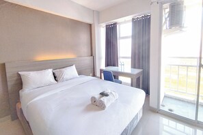 A hotel room with a large bed, a desk, and a view of the outdoors. - Restful And Best Location Studio At Taman Melati Surabaya Apartment (Surabaya)