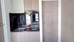 Μια μικρή κουζίνα με ξύλινα ντουλάπια, ένας ανοξείδωτος νεροχύτης και μια κόκκινη συσκευή.