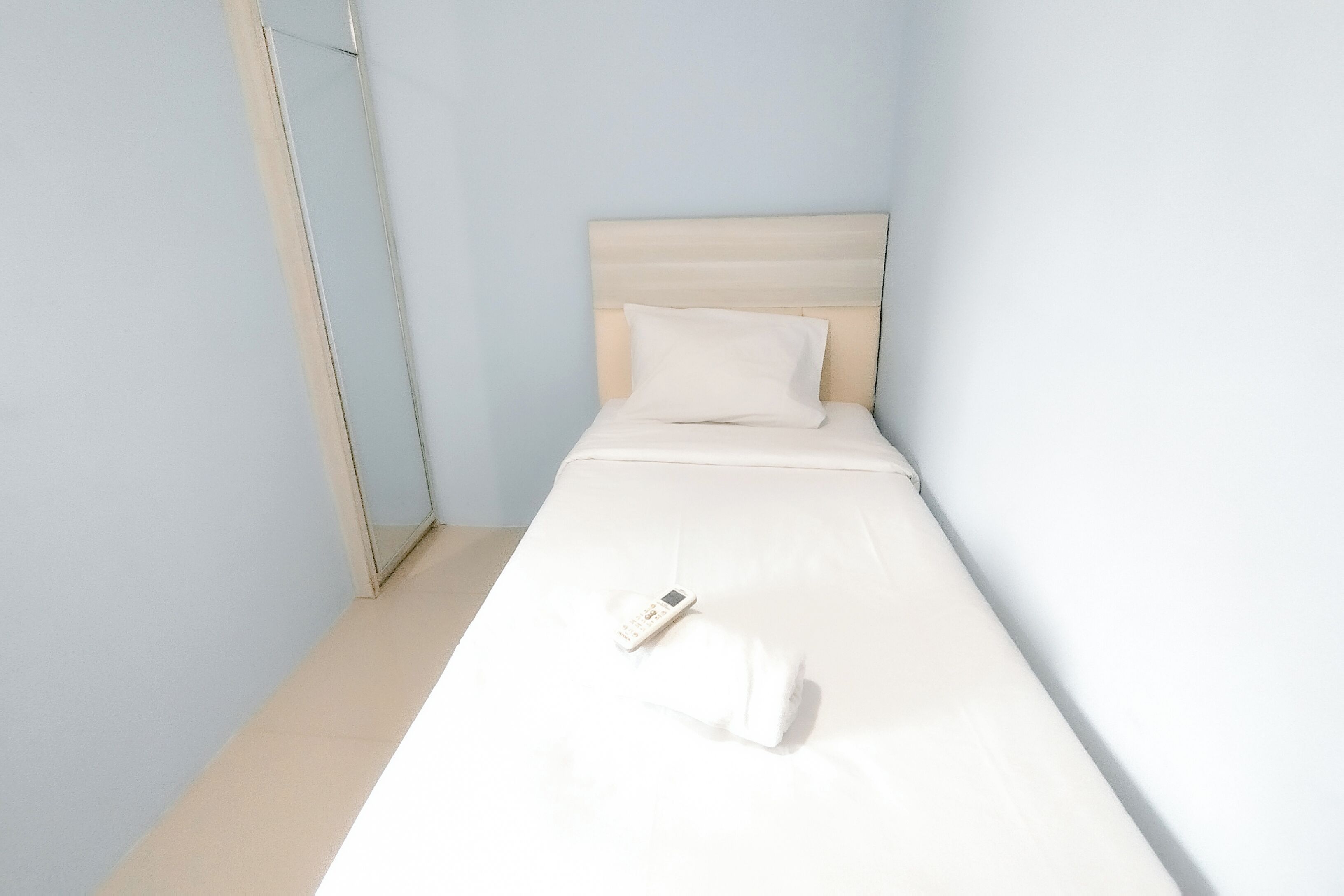 A small, single-bed room with a plain white headboard and a white pillow.