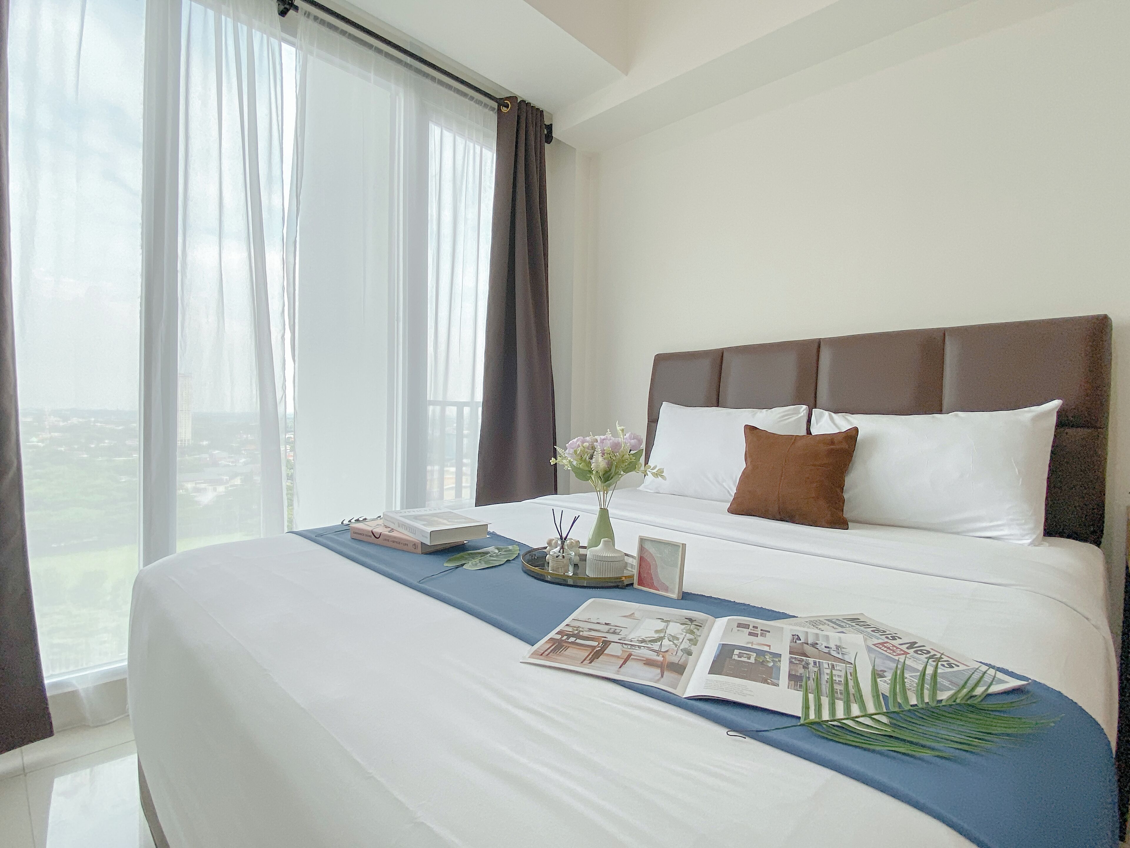 A hotel room with a large bed, a view of the city, and a window with sheer curtains.