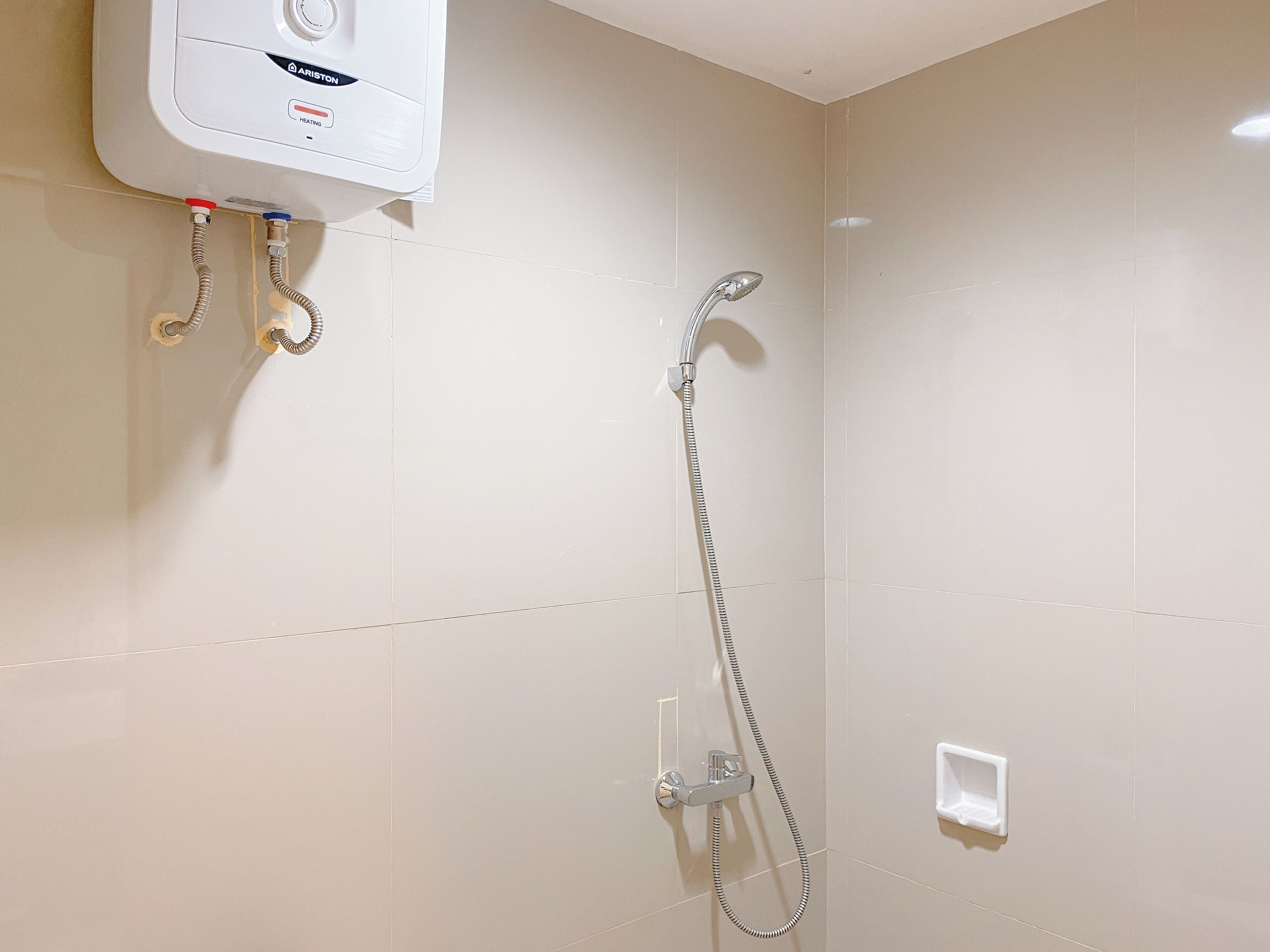 A bathroom with a wall-mounted heater, a showerhead, and a control panel.