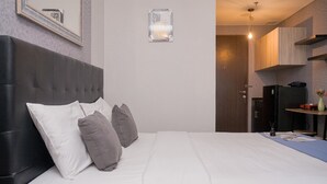 Habitación de hotel con una cama grande, un cabecero, una mesita con un florero y una puerta que da a una kitchenette.