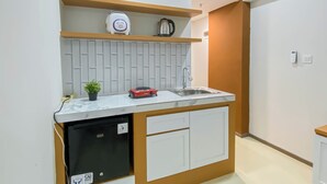 A compact kitchen with a built-in dishwasher, a sink, and a coffee maker on a shelf. - Cozy Living Studio Room At Meikarta Apartment (Cikarang)