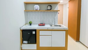 A compact kitchen with a built-in dishwasher, a sink, a small shelf with a kettle, and a potted plant. - Cozy Living Studio Room At Meikarta Apartment (Cikarang)