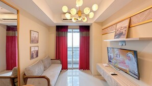 A modern living room with a sofa, a TV, and a large window with red curtains. - New Contemporary 2Br At Grand Sungkono Lagoon Apartment (Surabaya)