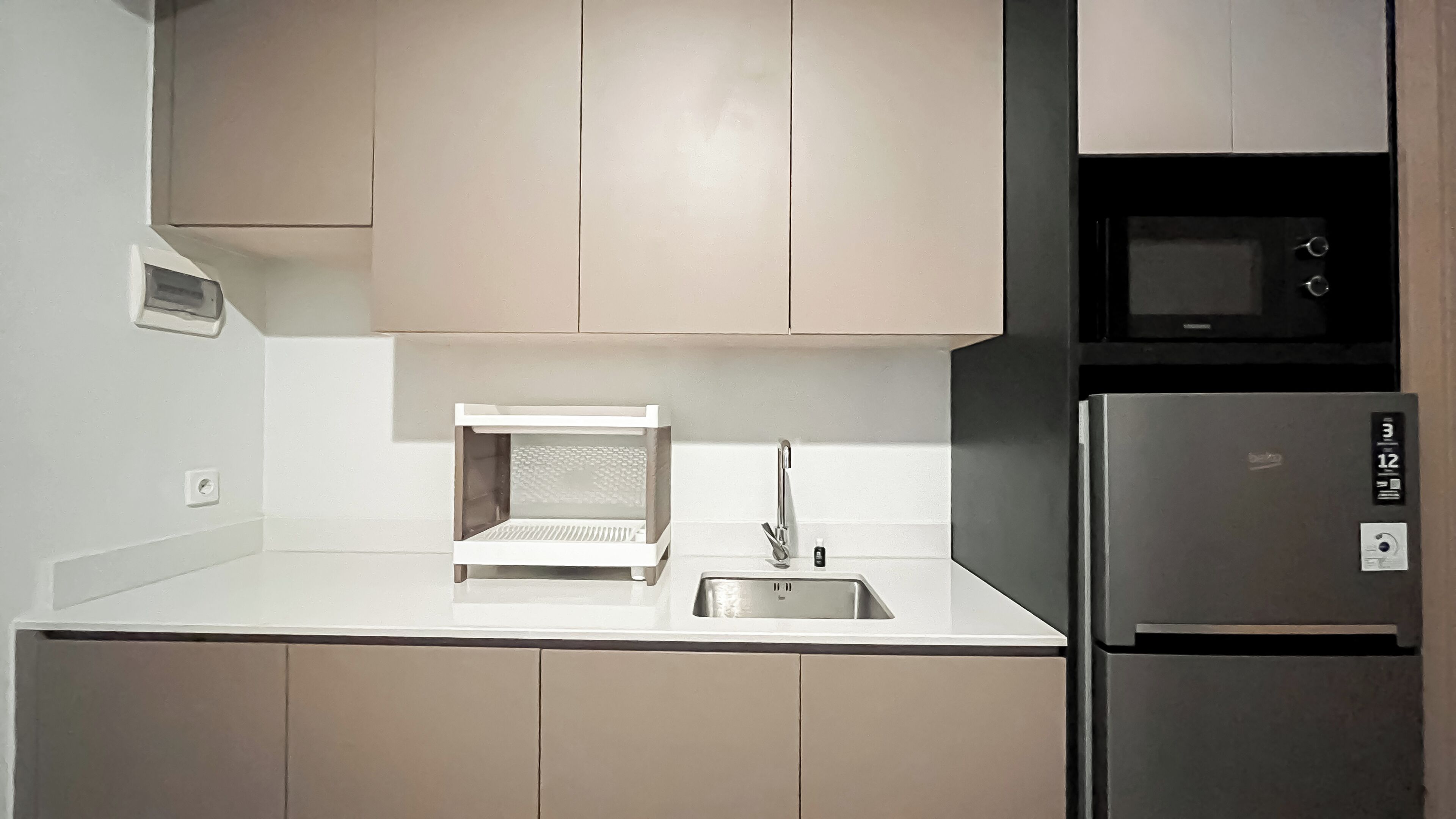 A modern kitchen with a built-in microwave, a stainless steel refrigerator, and a compact sink.