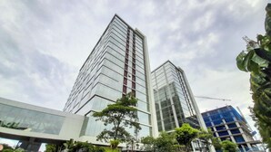 Two modern high-rise buildings with reflective glass facades, surrounded by greenery and under a partly cloudy sky.