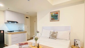 A hotel room with a bed, bedside table, a small kitchen area, and a painting on the wall. - Relaxing Studio Room At Meikarta Apartment (Cikarang)