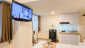 A hotel room with a bed, a TV mounted on the wall, a small kitchen area, and a window with curtains. - Relaxing Studio Room At Meikarta Apartment (Cikarang)