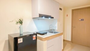 A compact kitchen with a black refrigerator, a sink, and a small countertop. - Relaxing Studio Room At Meikarta Apartment (Cikarang)