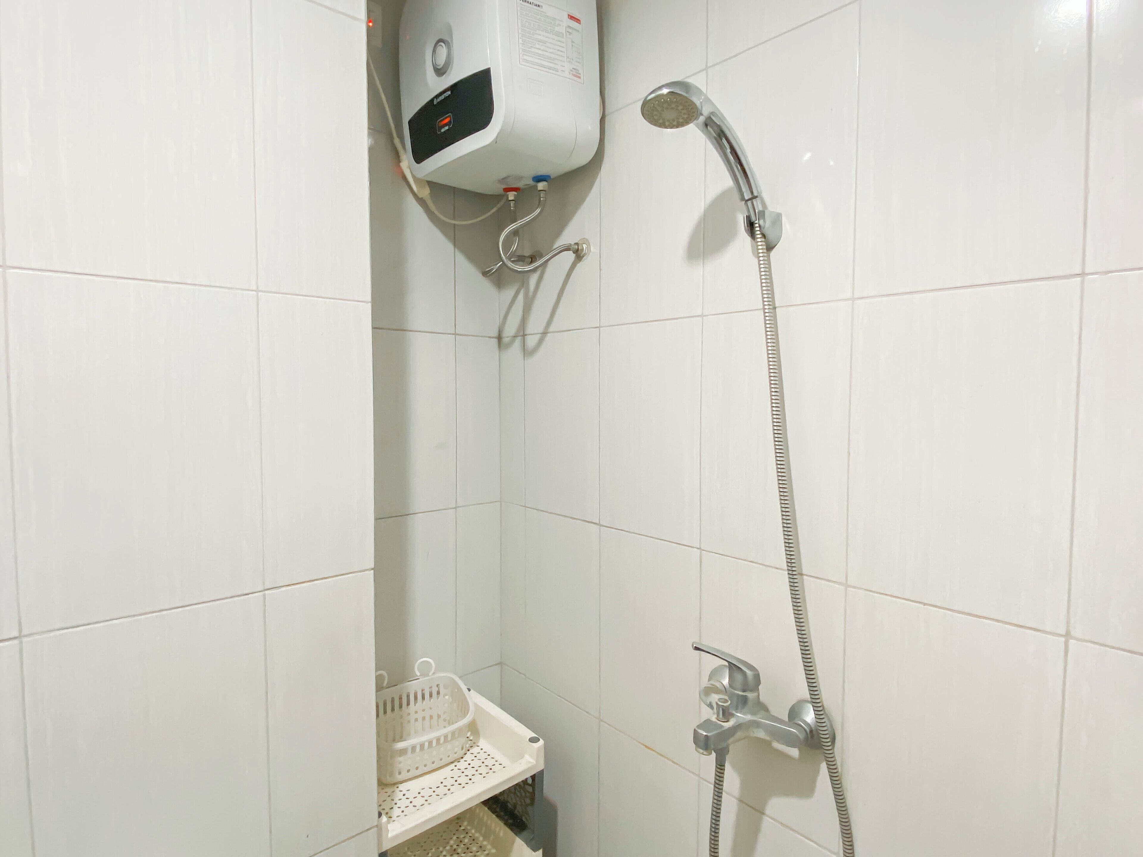 A bathroom with a shower, a hand dryer, and a small shelf with a basket.