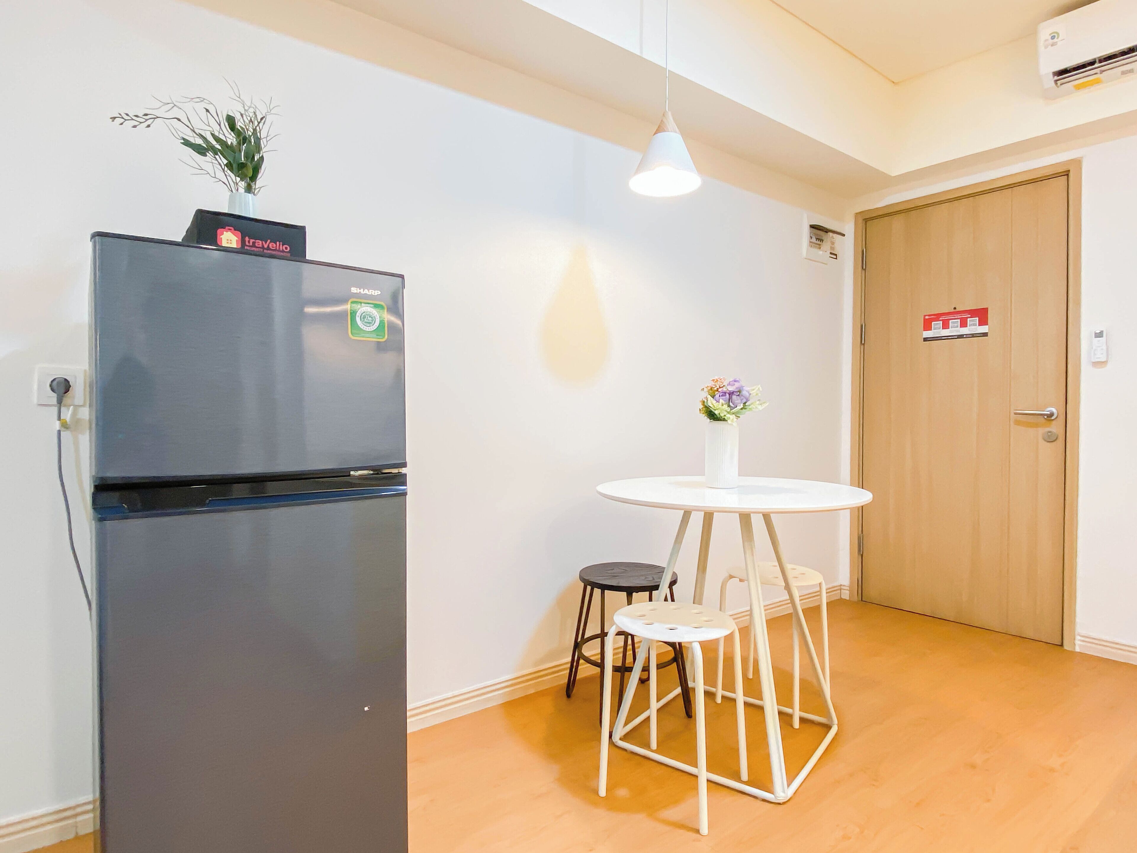 Una cocina compacta con un refrigerador negro, una pequeña mesa redonda con taburetes y una puerta de madera.