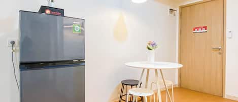 Una cocina compacta con un refrigerador negro, una pequeña mesa redonda con taburetes y una puerta de madera.