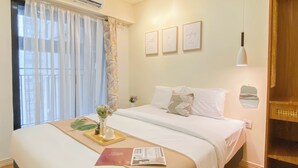 Een hotelkamer met een bed, een raam met gordijnen, een airconditioning en afbeeldingen in lijsten aan de muur.