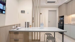 Une cuisine moderne avec un plan de travail blanc, deux tabourets de bar, un distributeur d’eau et un réfrigérateur.