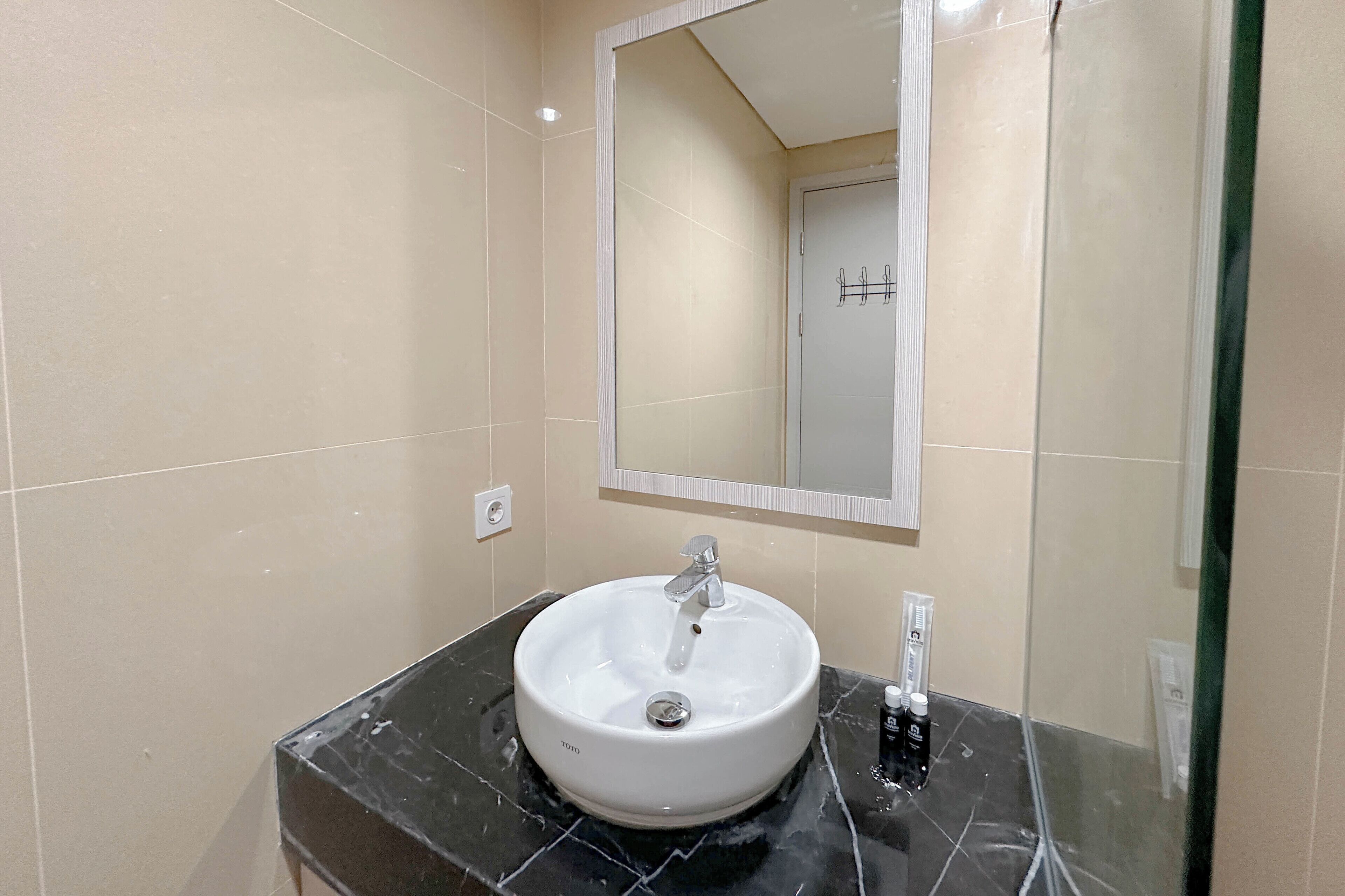 Un baño con lavamanos blanco, espejo y encimera de mármol negro.