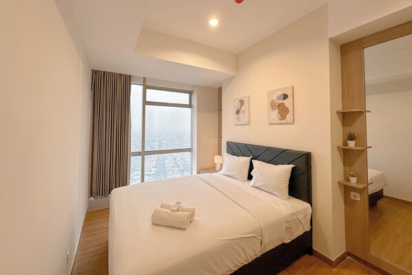 A hotel room with a large bed, a view of the city, and a modern design. - Stunning And Simply 2Br At Grand Sungkono Lagoon Apartment (Surabaya)