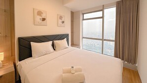 A modern hotel room with a large bed, a view of the city through a large window, and two pieces of wall art. - Stunning And Simply 2Br At Grand Sungkono Lagoon Apartment (Surabaya)