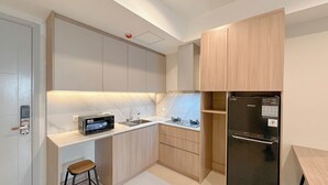 A modern kitchen with a built-in microwave, two sinks, a refrigerator, and a wooden stool. - Stunning And Simply 2Br At Grand Sungkono Lagoon Apartment (Surabaya)
