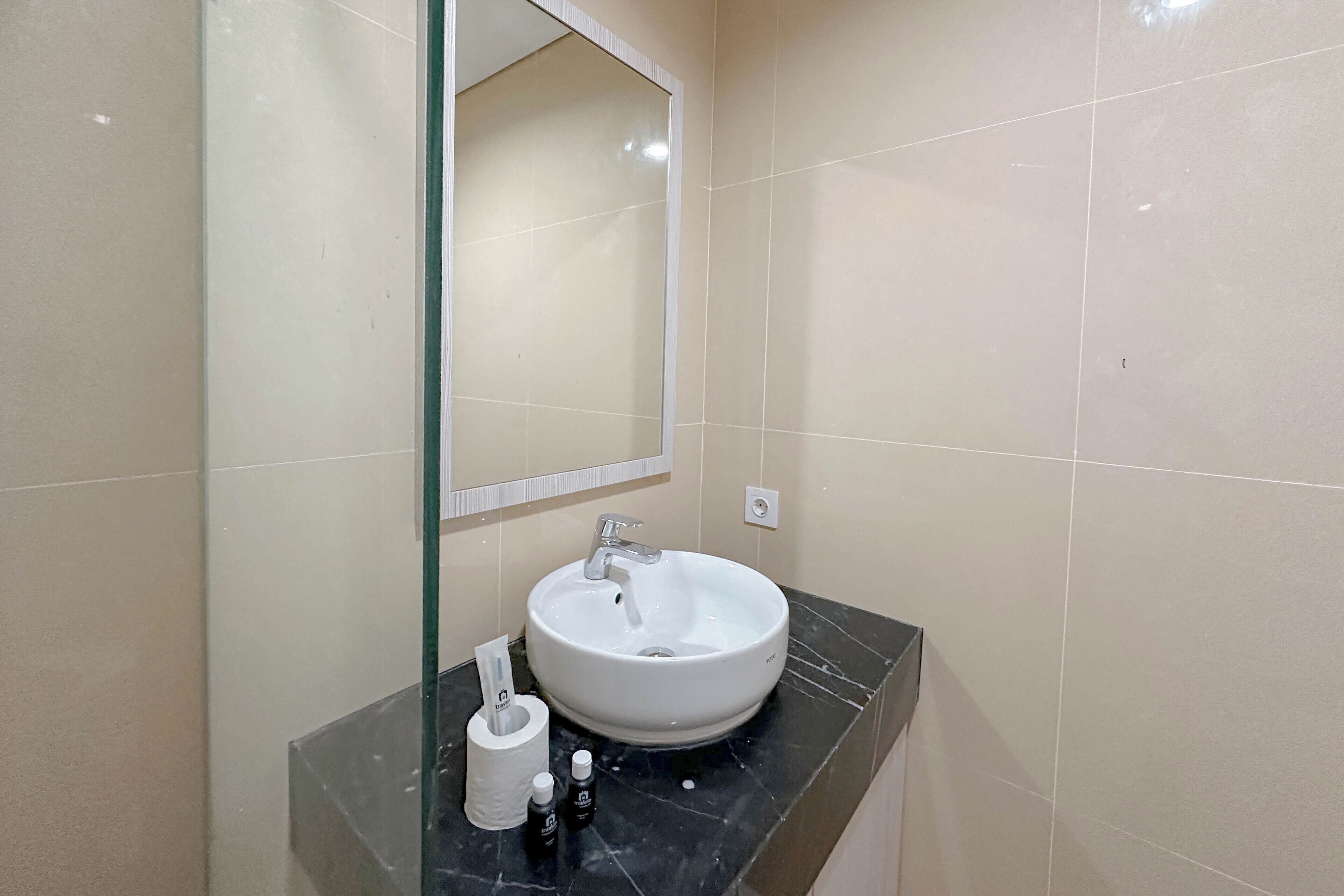 A bathroom with a white sink, a mirror, and toiletries on a black countertop.