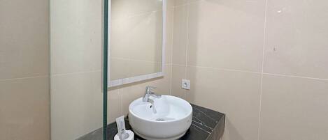 A bathroom with a white sink, a mirror, and toiletries on a black countertop.