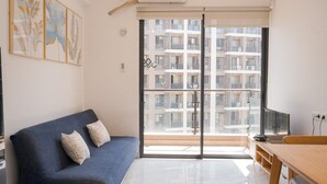 Un salon moderne comprenant un canapé, une table à manger et une grande fenêtre donnant sur un immeuble d’habitation.